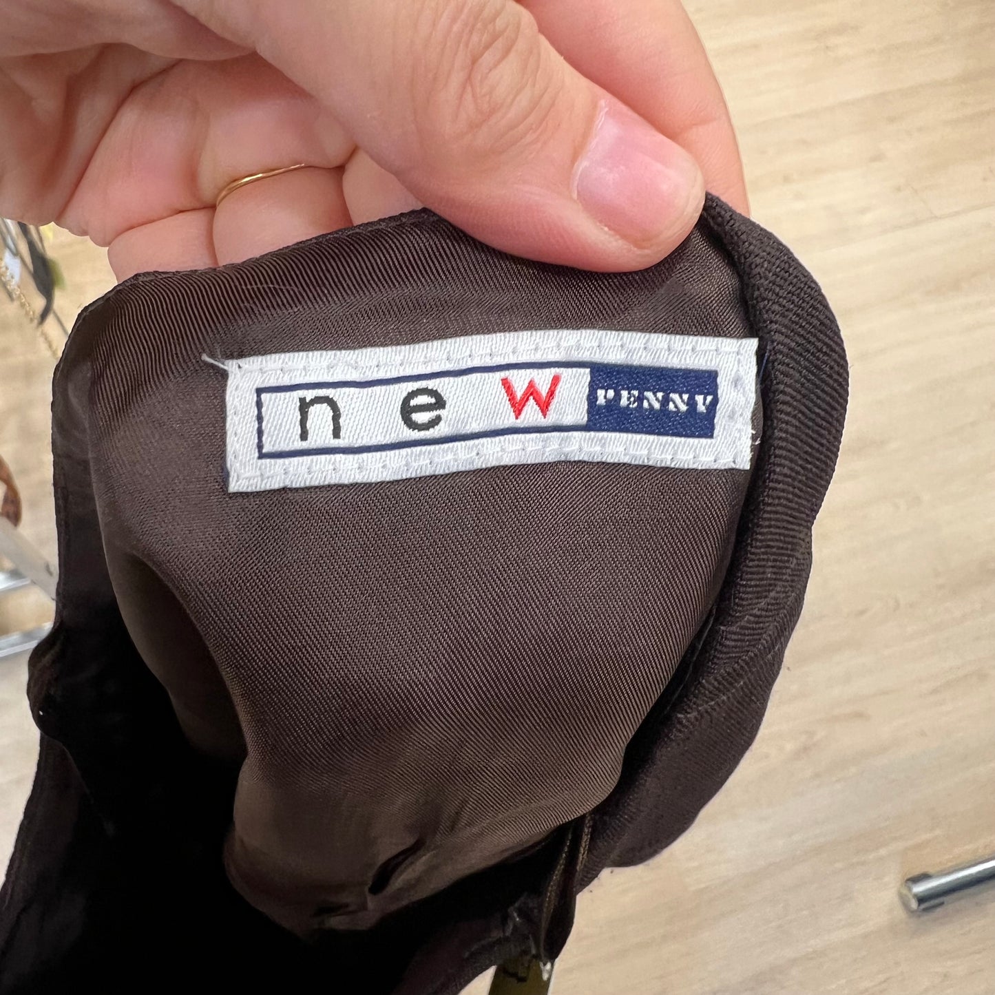 Brown fabric with a 'New Penny' label held by a hand on a wooden surface