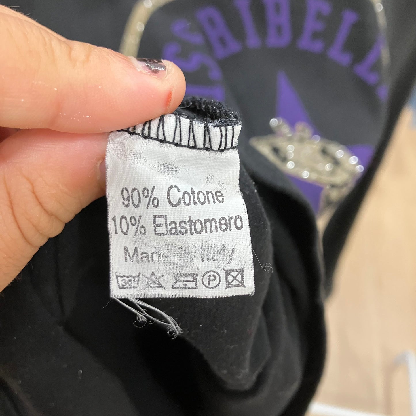 Clothing label with text on a black garment, brand visible in the background