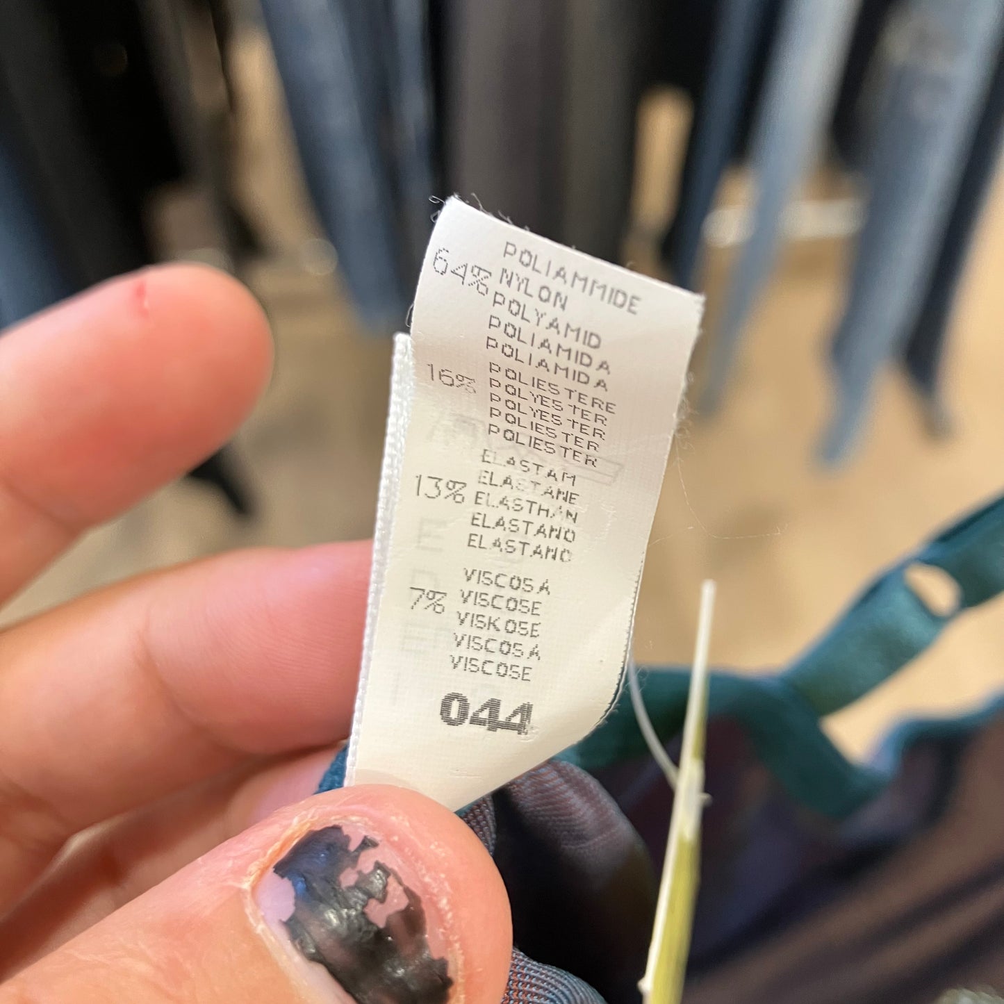 Close-up of a clothing tag with text held by a hand, blurred background