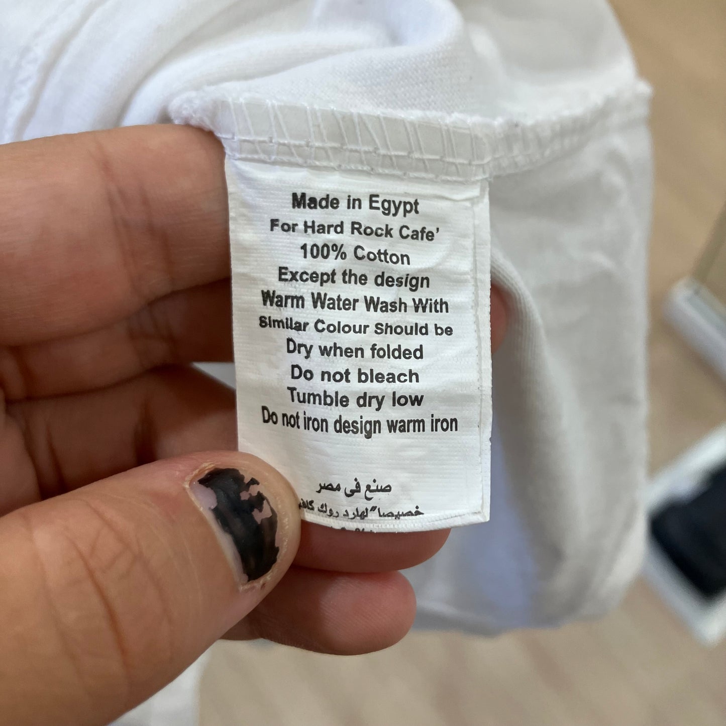 Clothing label held by a hand with text on it, against a blurred background