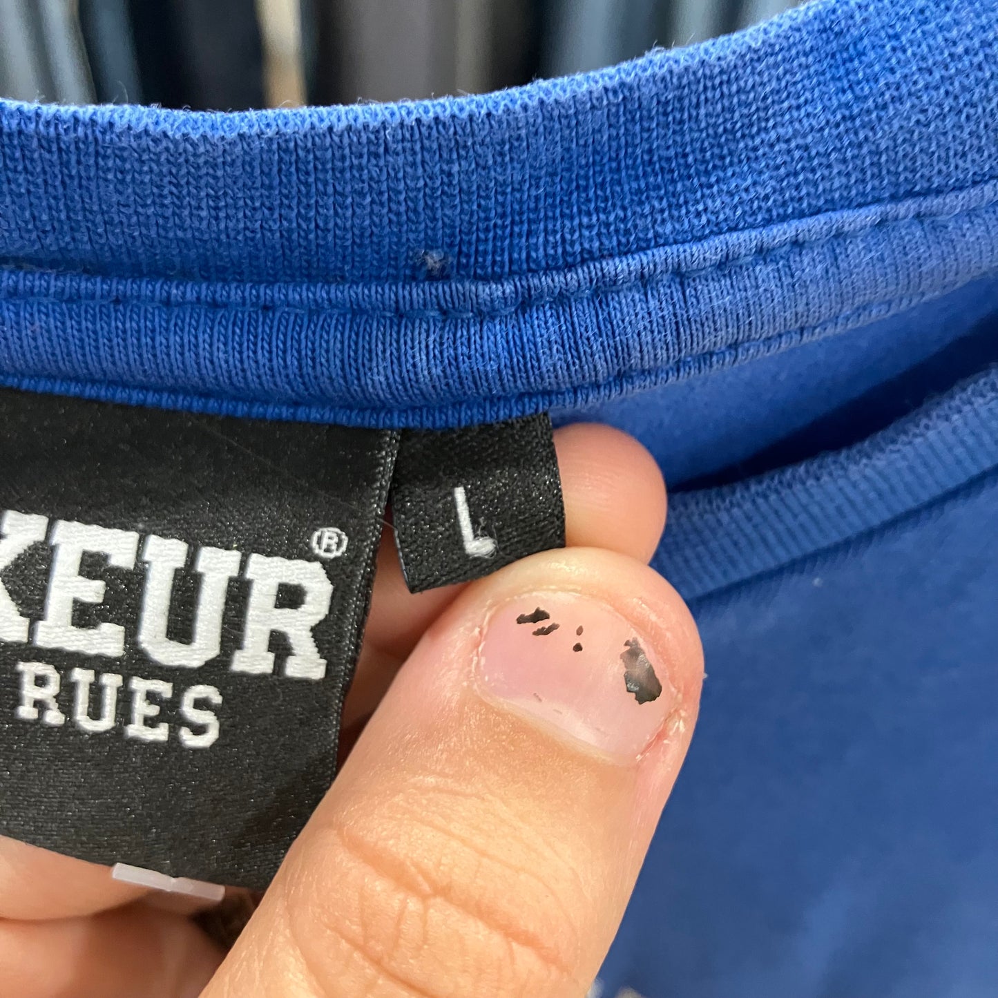 Close-up of a blue garment with a size label 'L' held by a hand