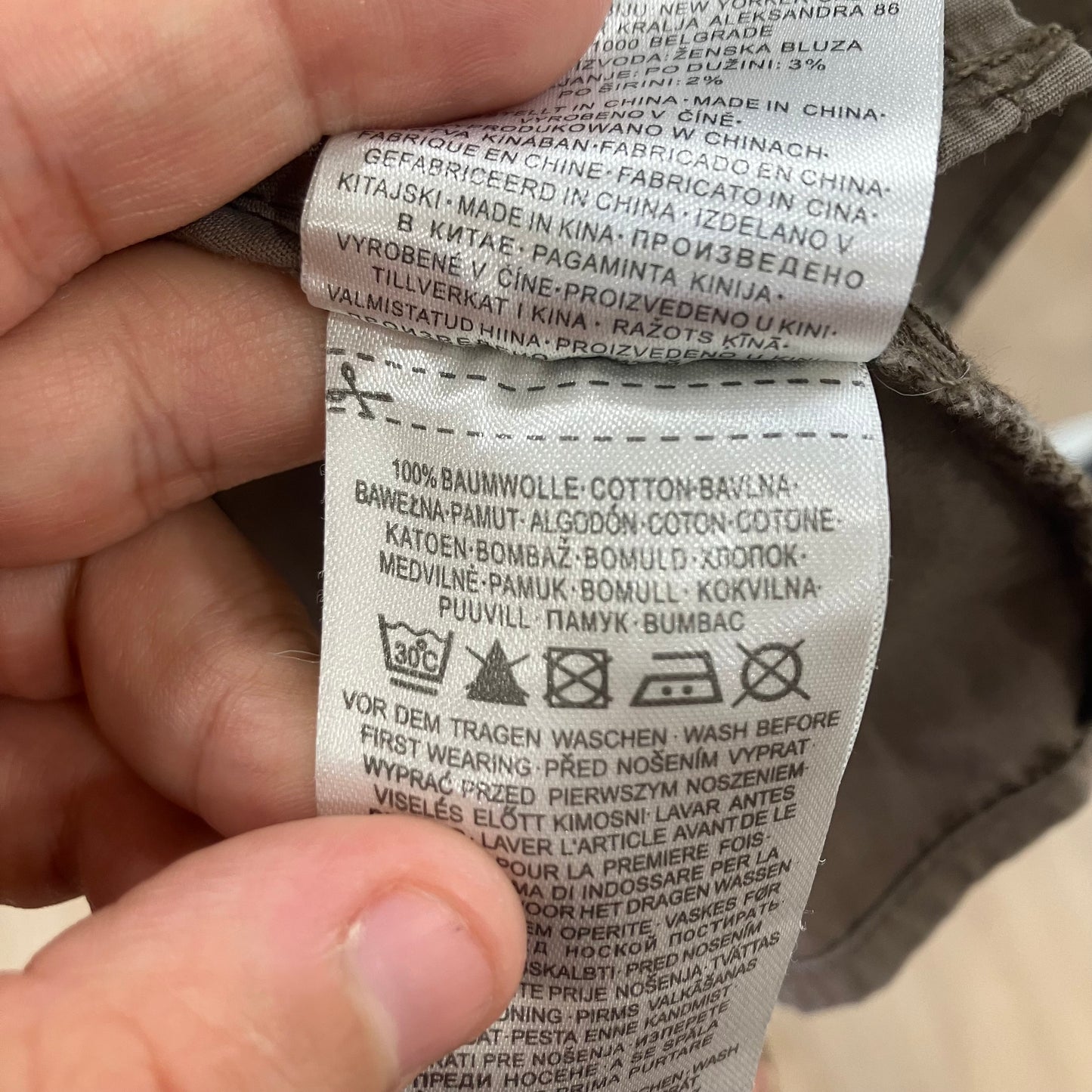 Close-up of a clothing label held by a hand, with text and symbols on it