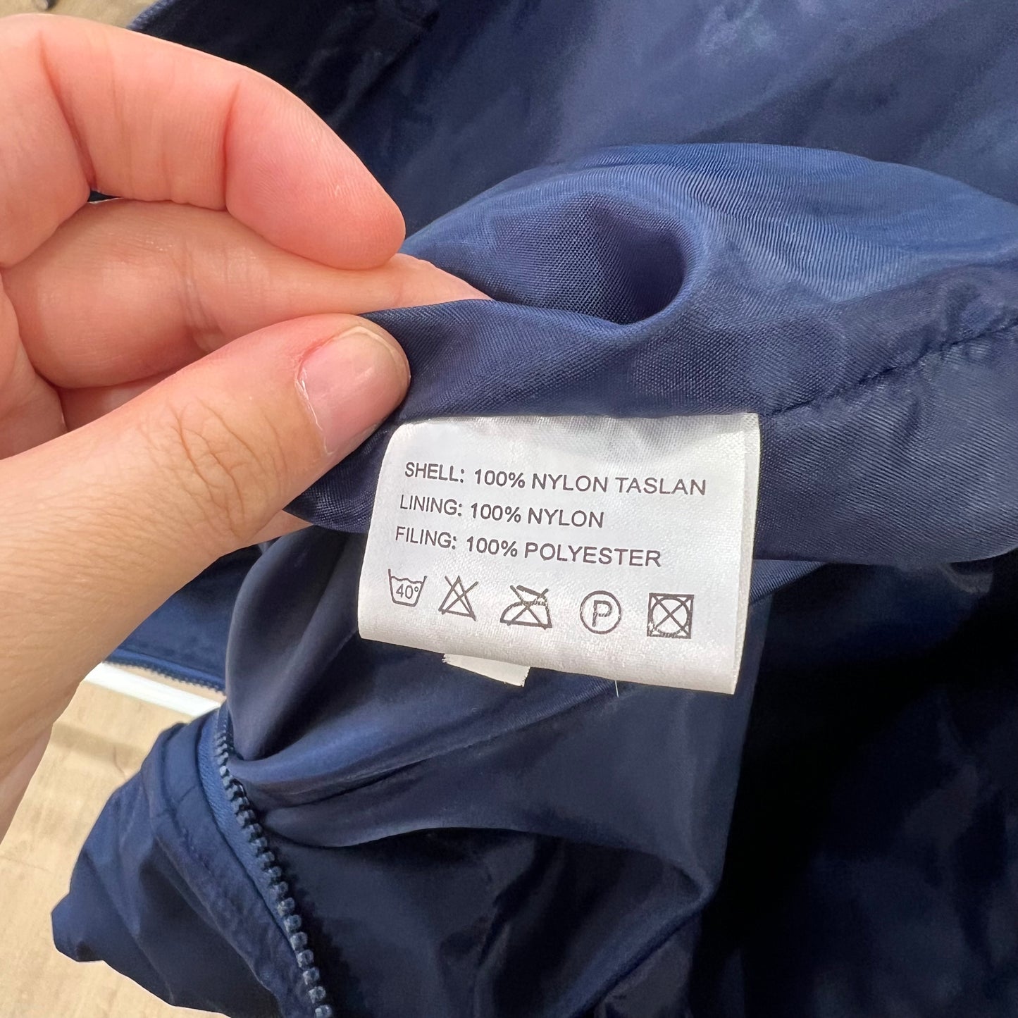 Hand holding a clothing label on a blue jacket with text and symbols