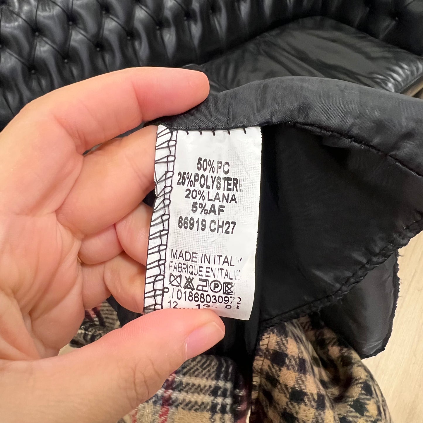 Hand holding a clothing label on a black jacket with plaid lining
