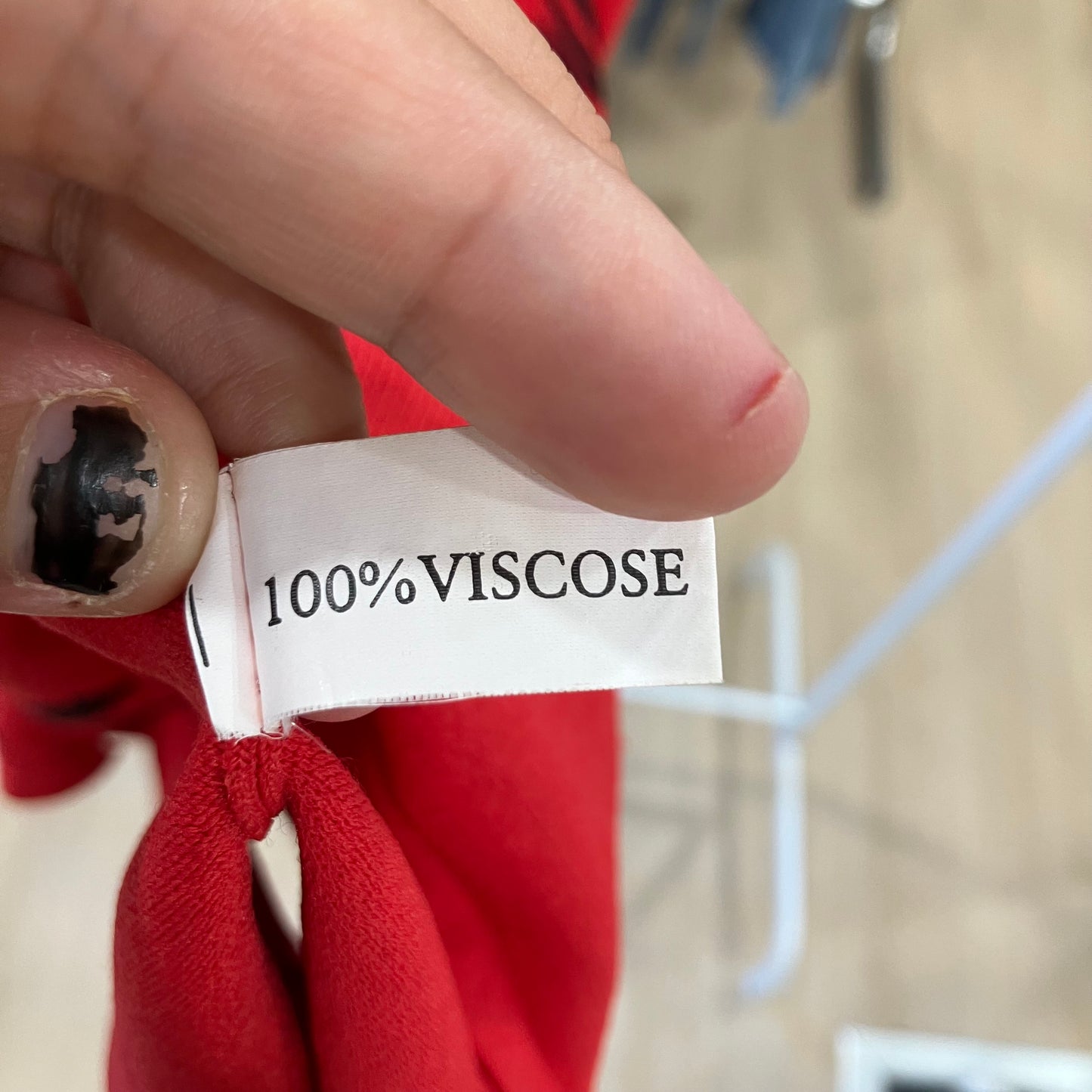 Hand holding a label with '100% Viscose' text on a red fabric background