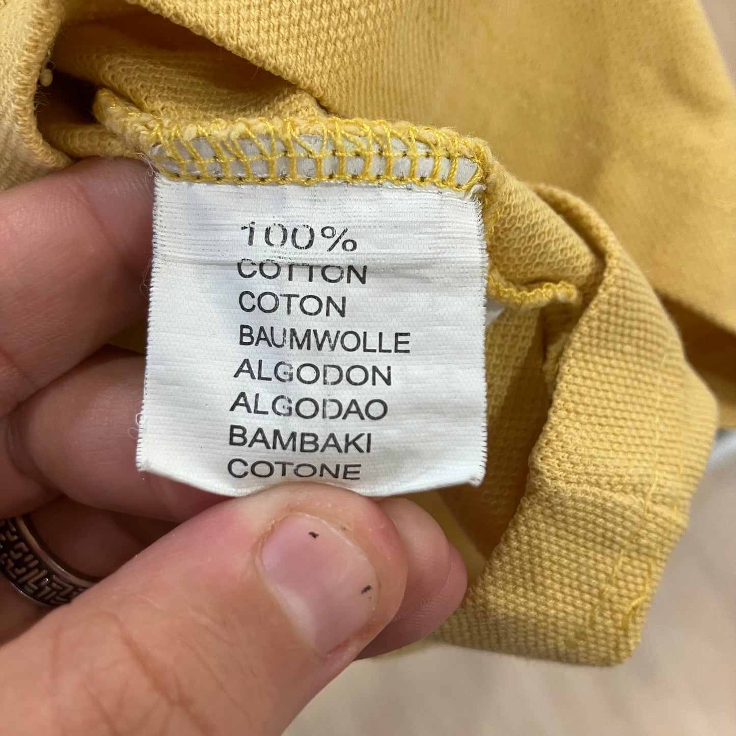 Close-up of a yellow fabric with a '100% Cotton' label held by a hand