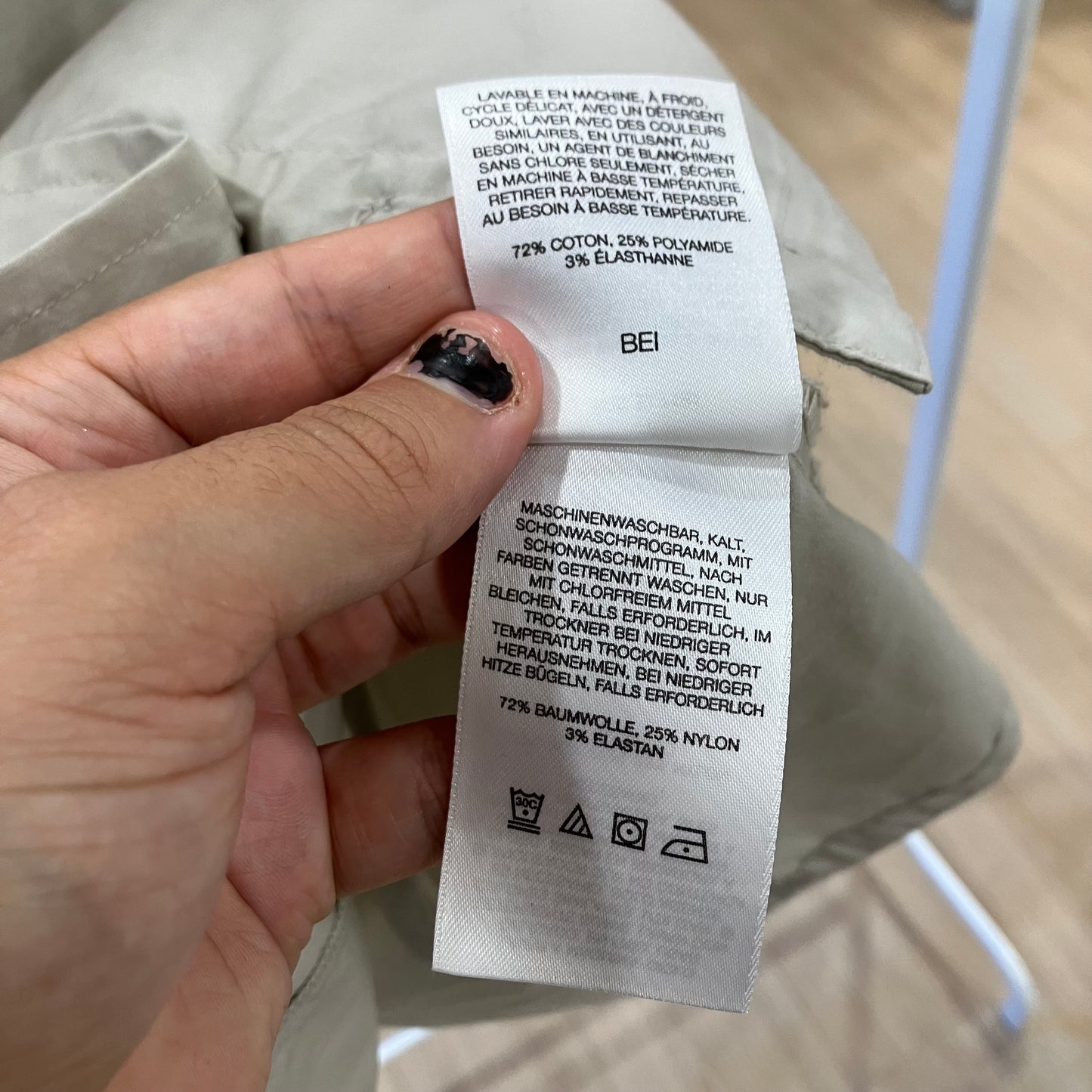 Hand holding a clothing label with text and symbols on a beige garment