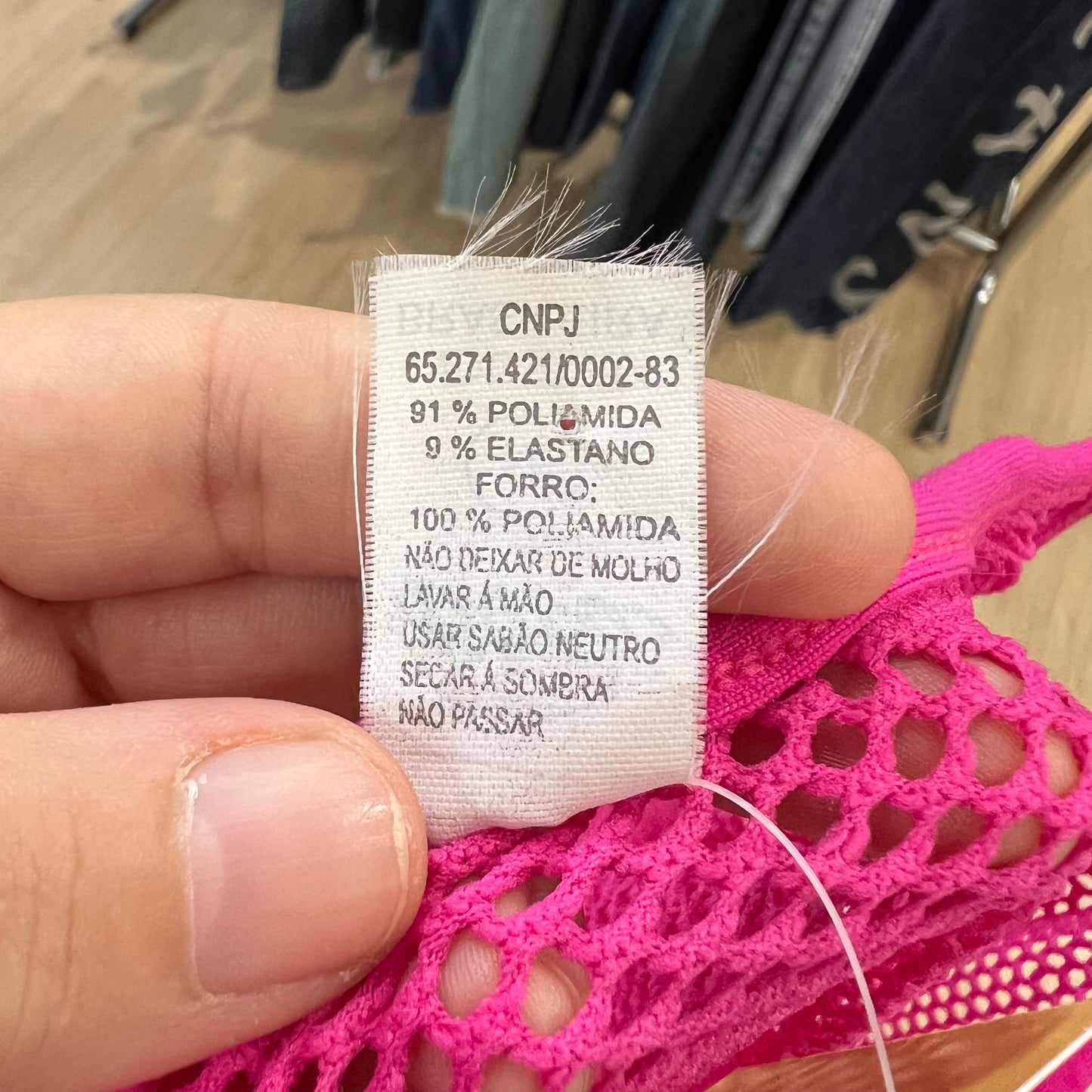 Clothing label held by a hand with pink lace fabric in the background