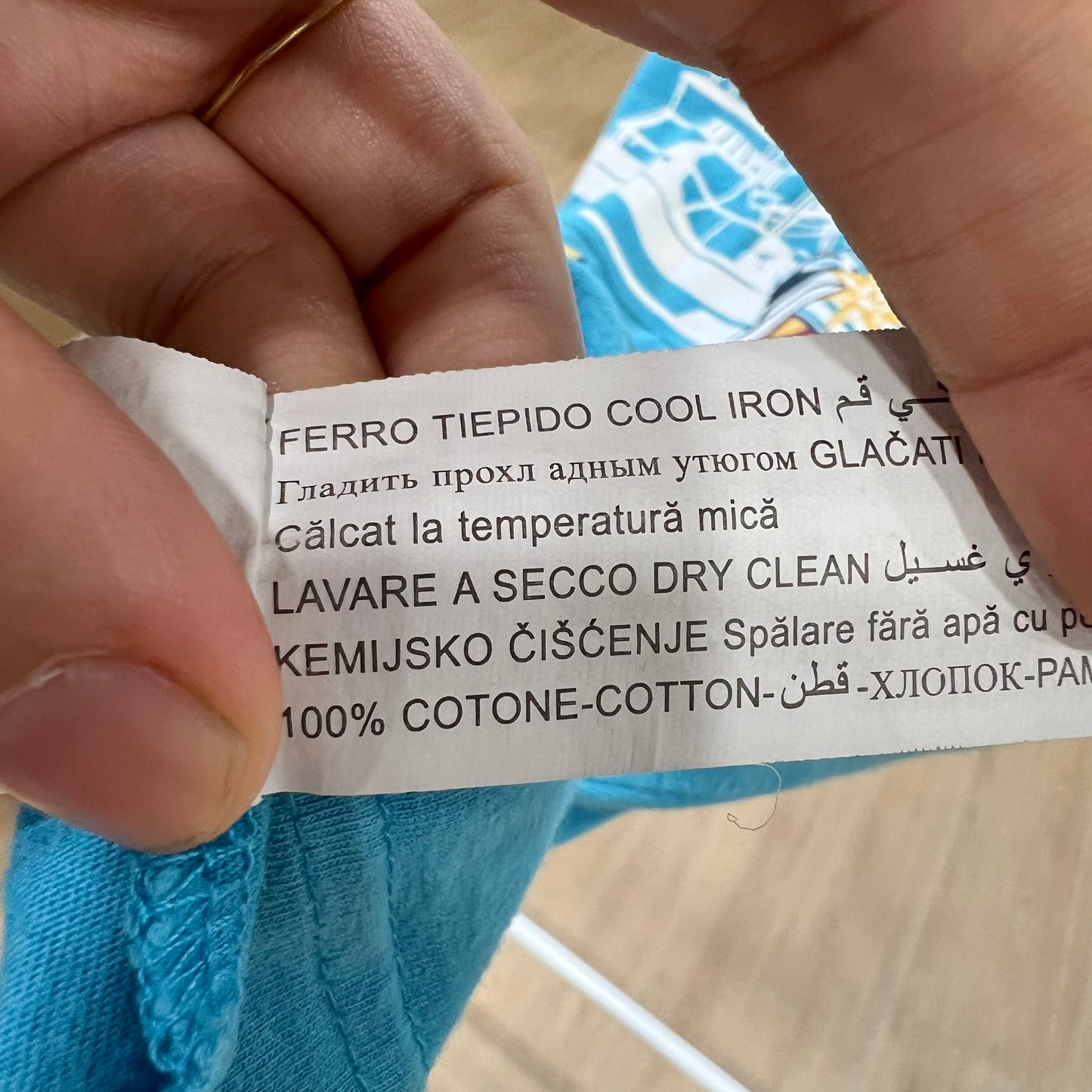 Clothing label held by a hand with text on it, against a blurred background.