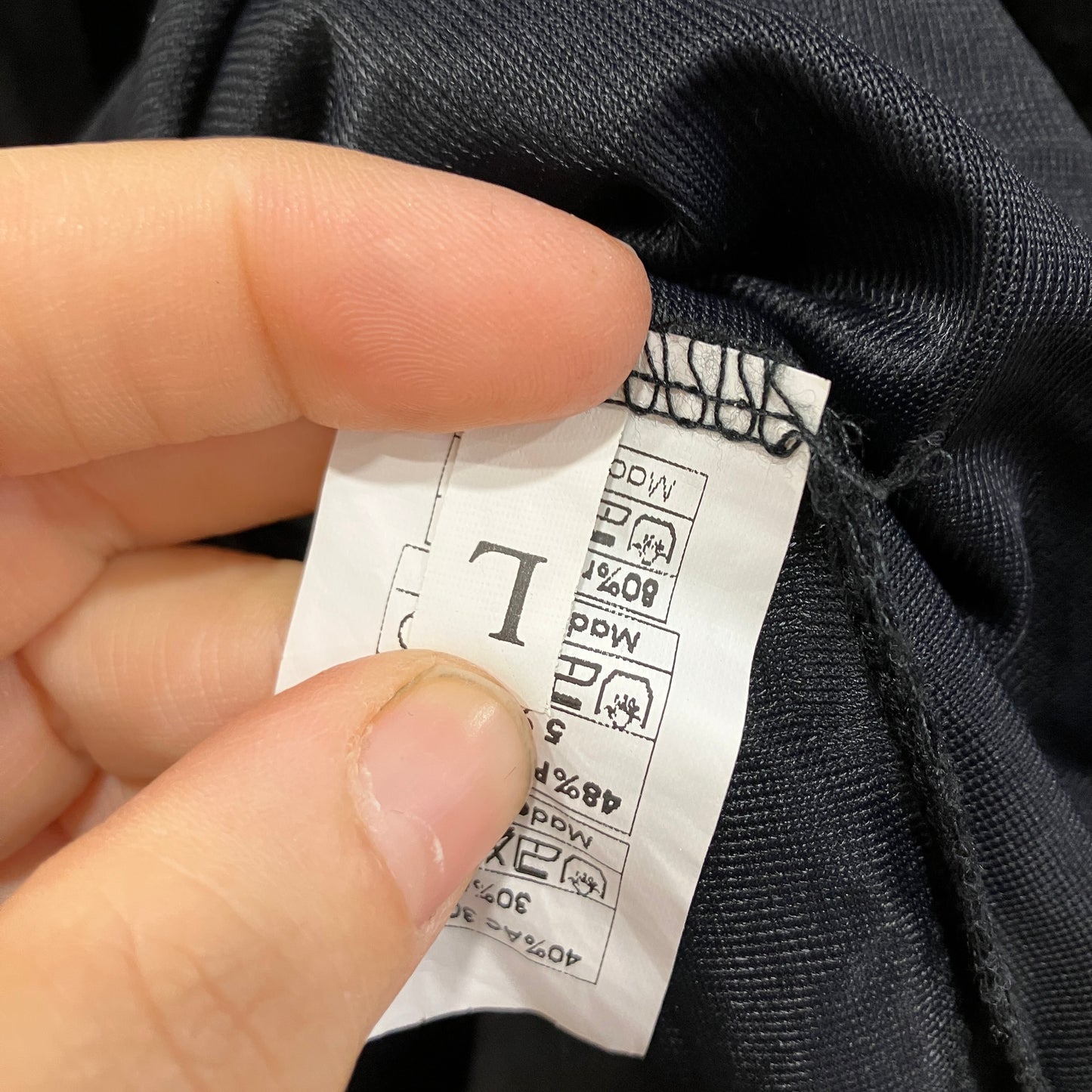 Hand holding a clothing label against dark fabric