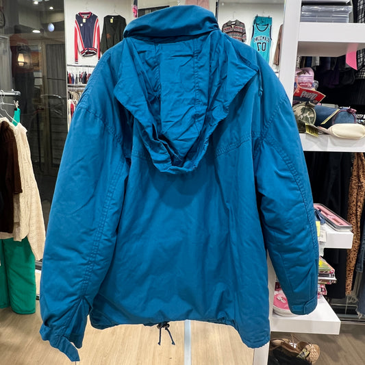 Back view of a teal hooded winter jacket with relaxed fit and drawstring hem, displayed on a hanger inside a vintage clothing store