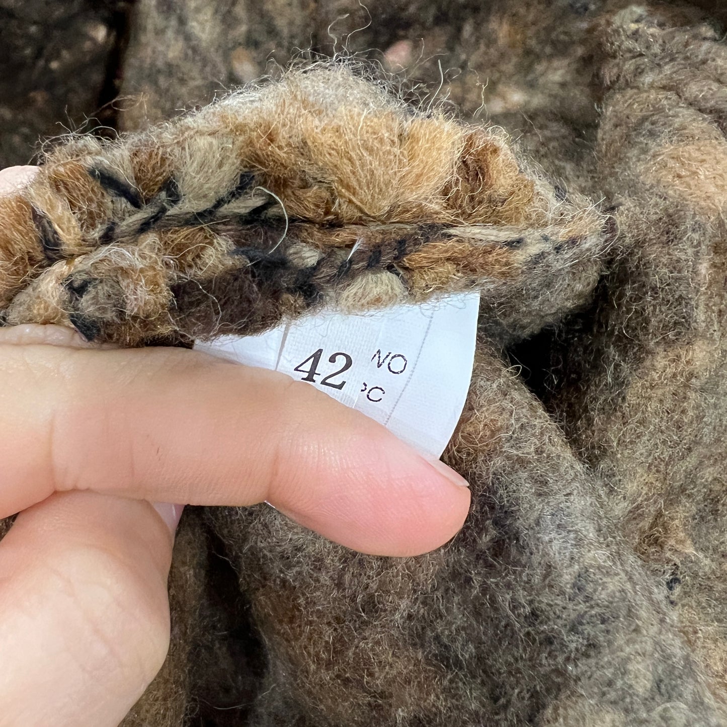 Close-up of a hand holding a piece of brown fabric with a size tag