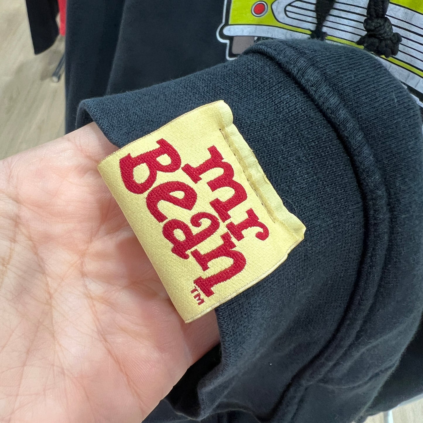 Hand holding a patch with 'Mr Bean' text on a dark fabric background