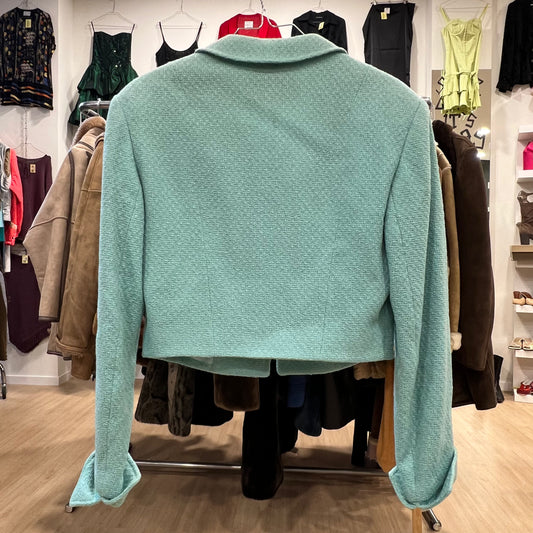 Light turquoise cropped blazer with long sleeves and a textured fabric, displayed on a rack in a vintage clothing store