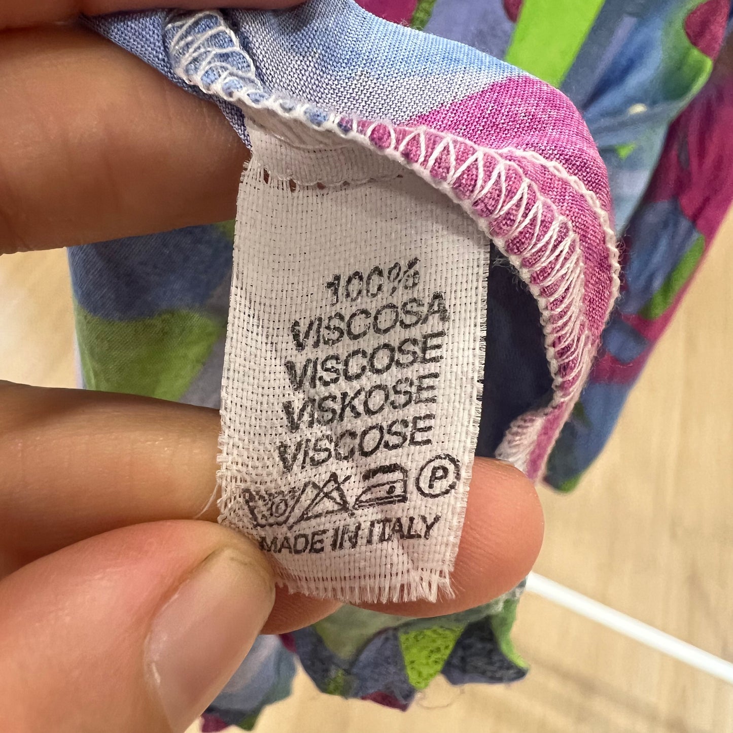 Fabric label with text '100% Viscose' held by a hand against a colorful background