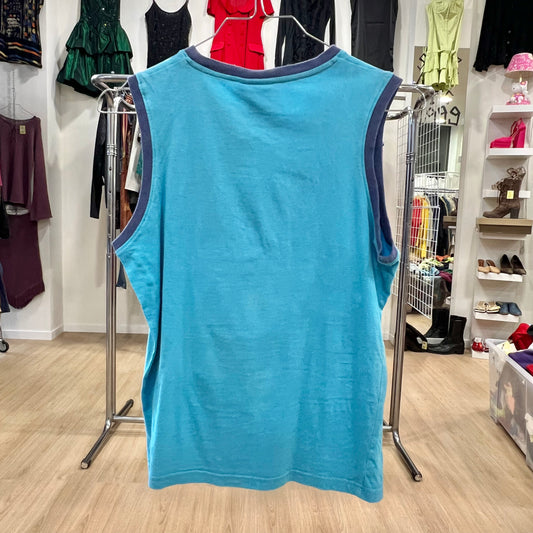 Blue sleeveless shirt on a hanger in a store setting with various clothing items in the background.