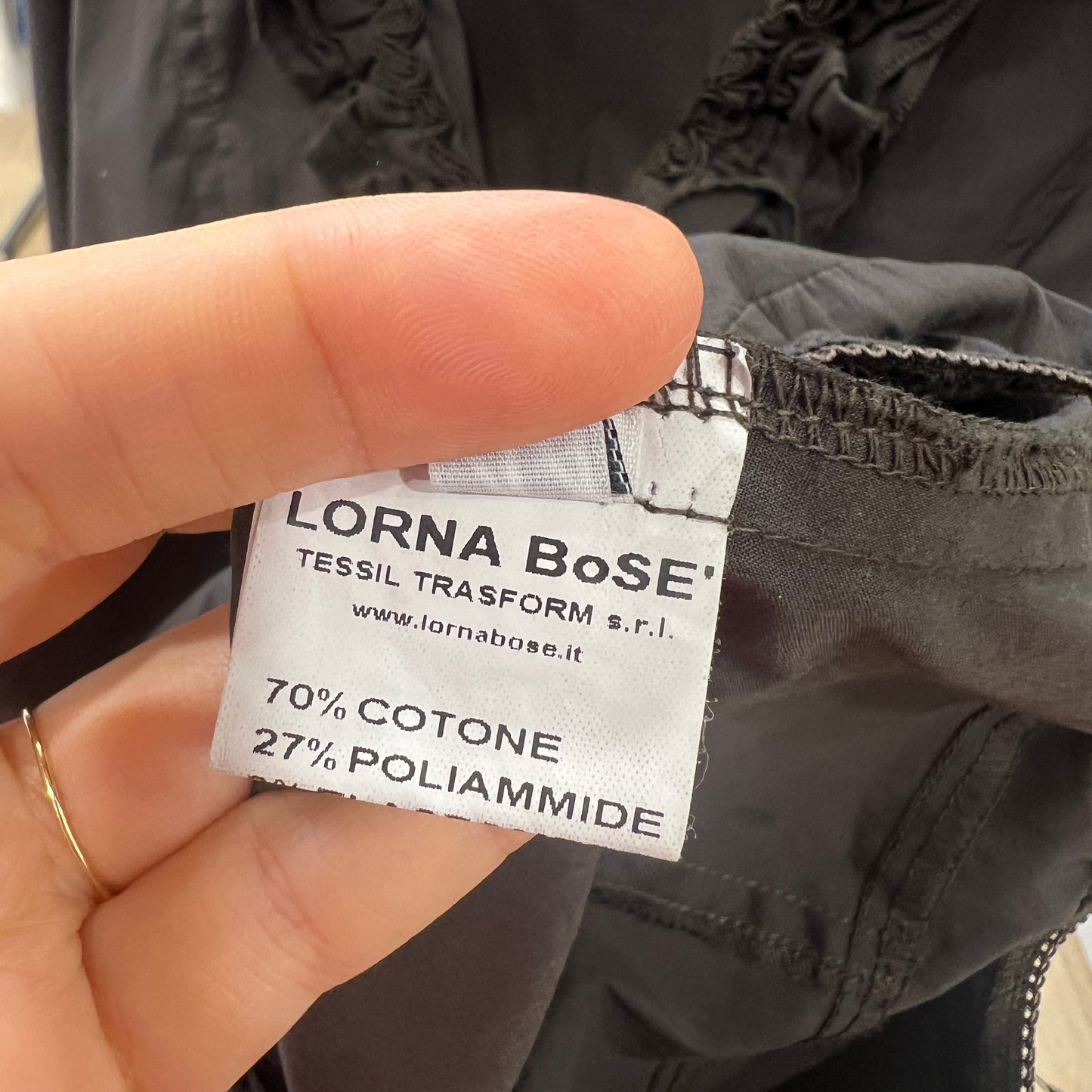 Hand holding a label on a black garment with 'LORNA BoSE' branding
