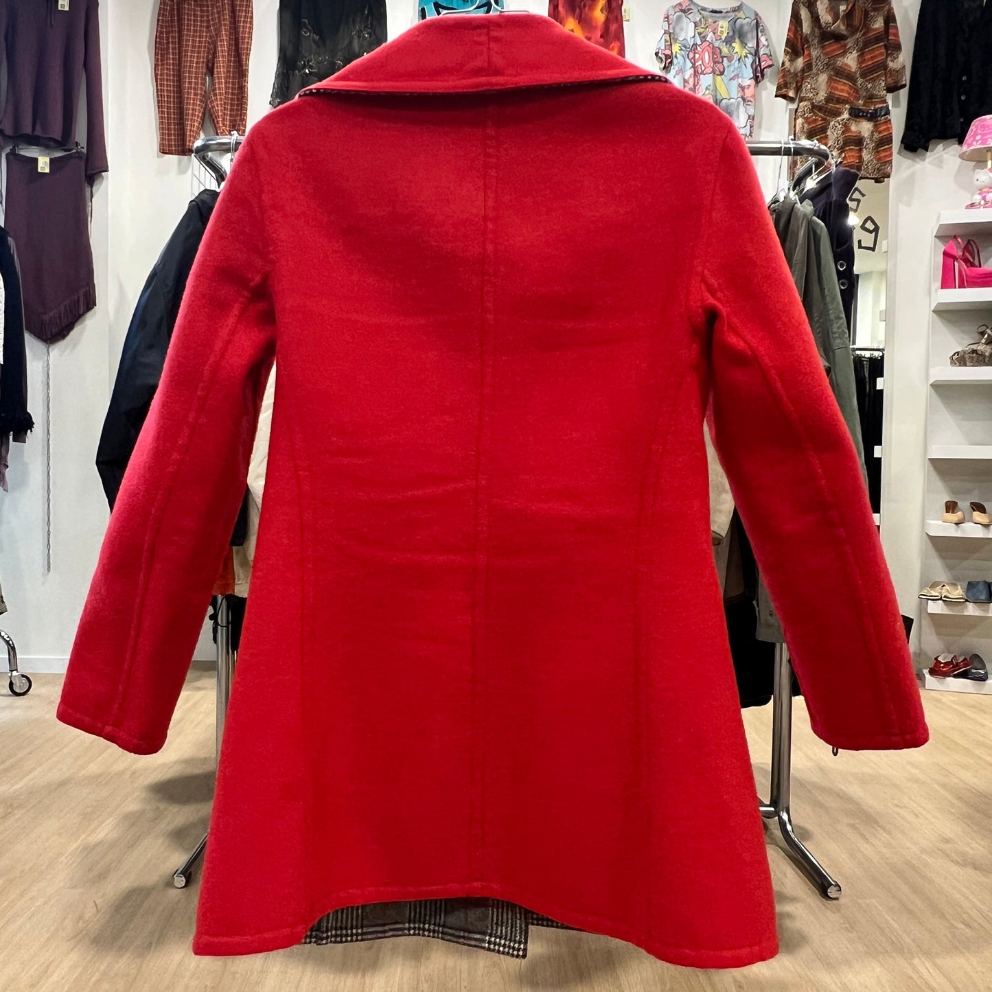 Red coat displayed in a store setting with racks of clothes in the background