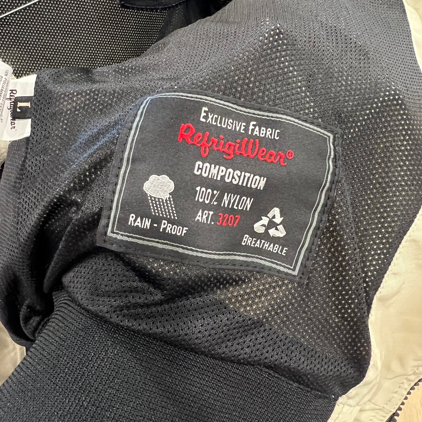Close-up of a RefrigiWear inner label on a black mesh lining, showing composition 100% nylon, rain-proof and breathable features, and art. 3207