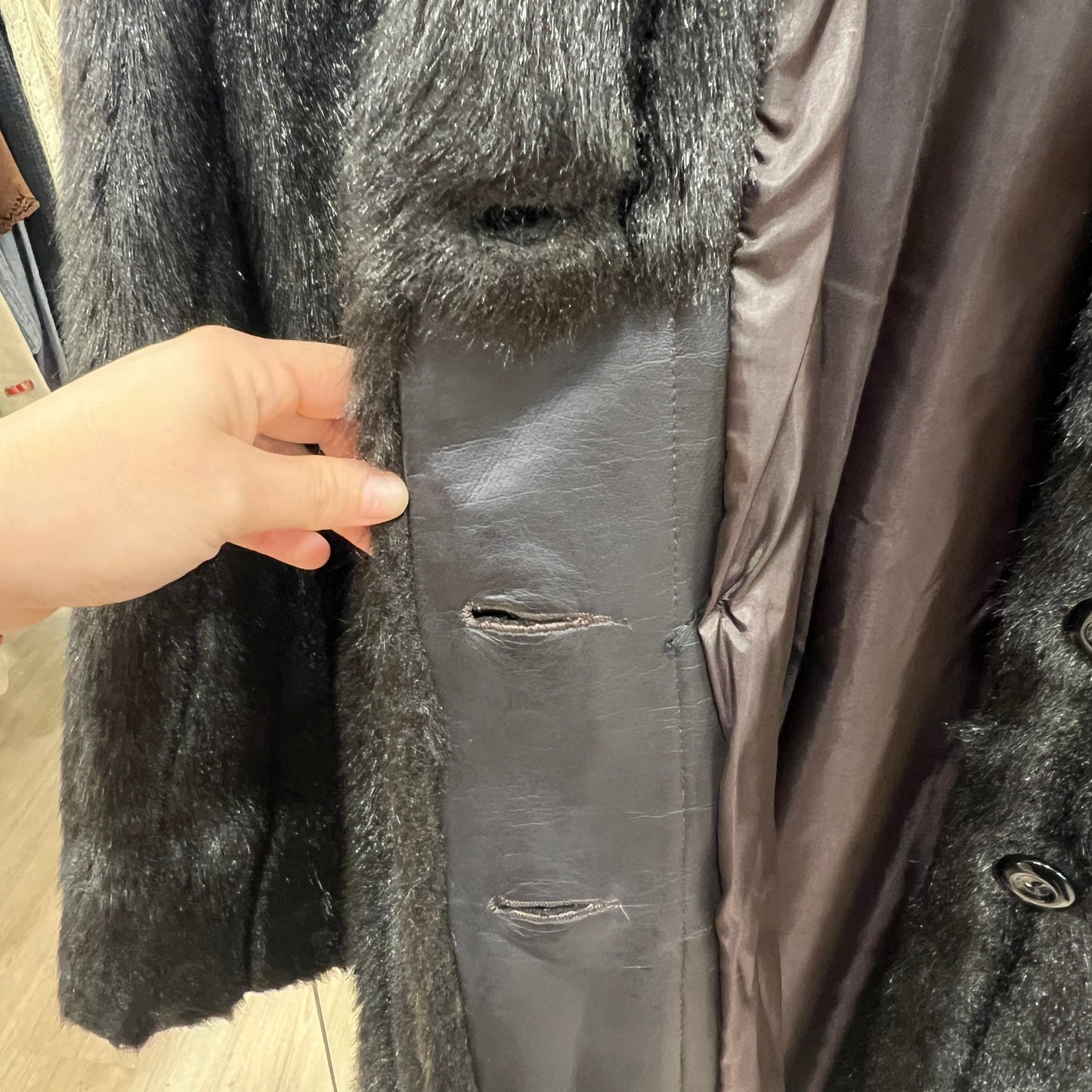 Close-up of a dark coat with a hand pointing to a tear, on a wooden floor