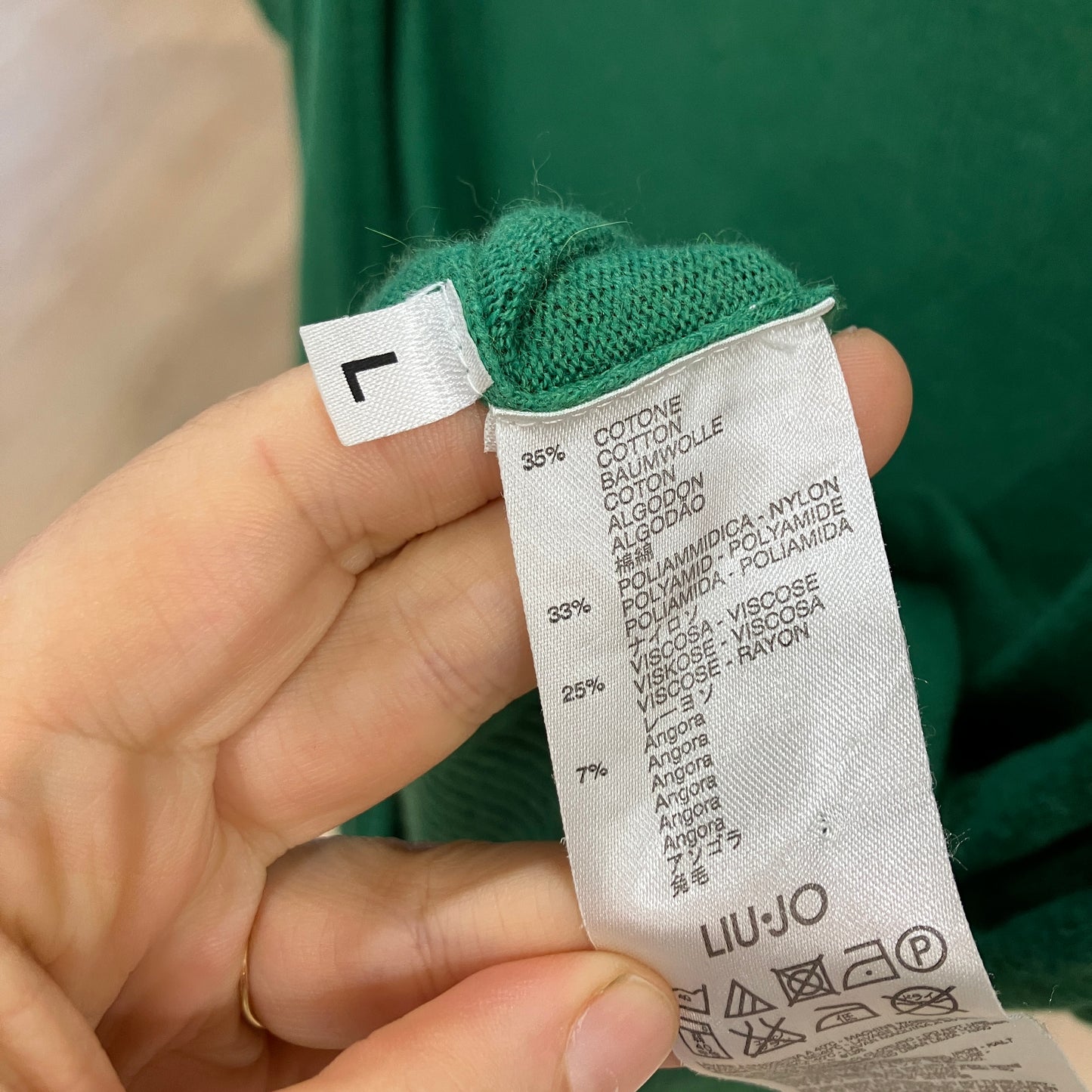Clothing label with fabric composition details held by a hand against a green background