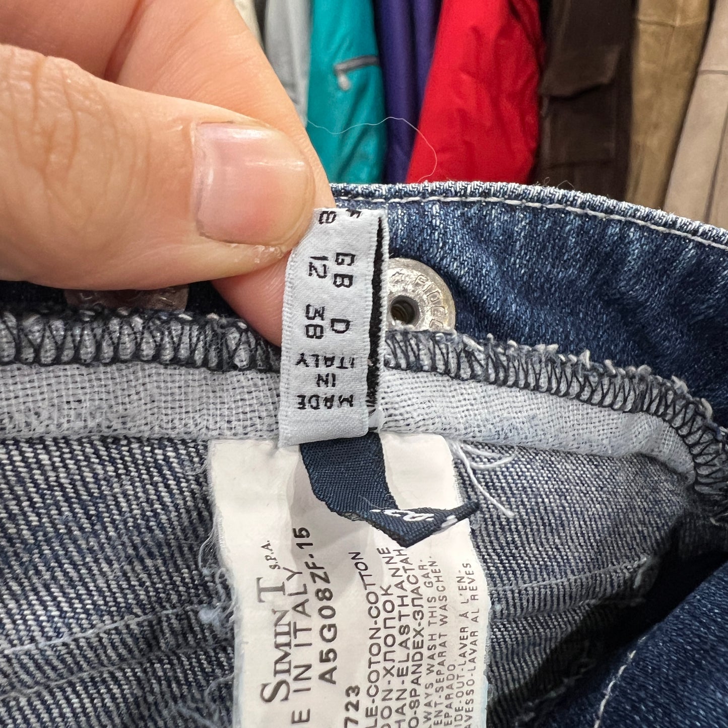 Close-up of a hand holding the inner size tag of blue denim jeans with visible stitching and size conversions