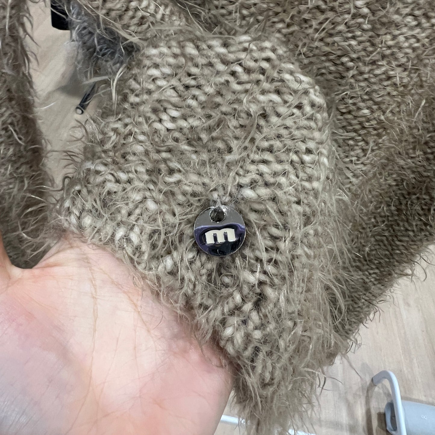 Textured beige fabric with a small M charm held by a hand