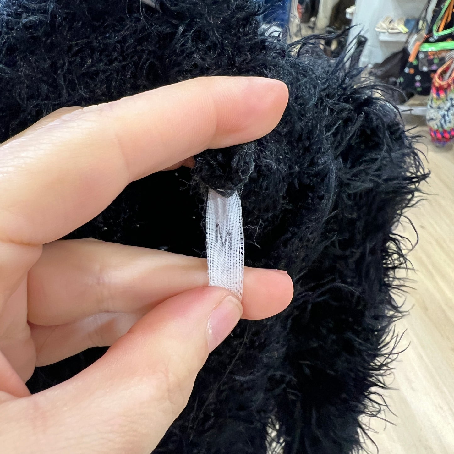 Hand holding a black furry coat with a visible brand tag