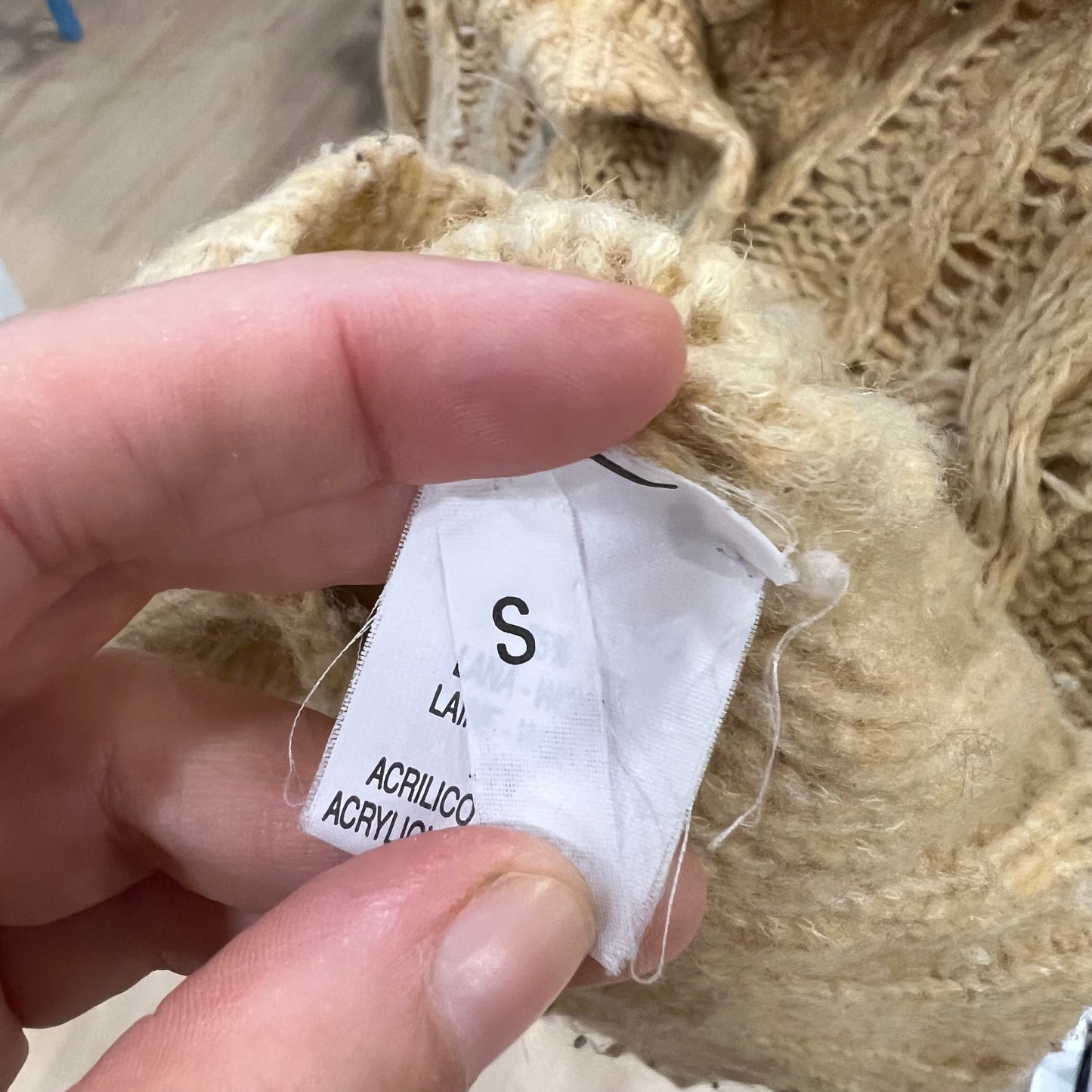 Hand holding a fabric tag with size 'S' on a textured beige fabric background