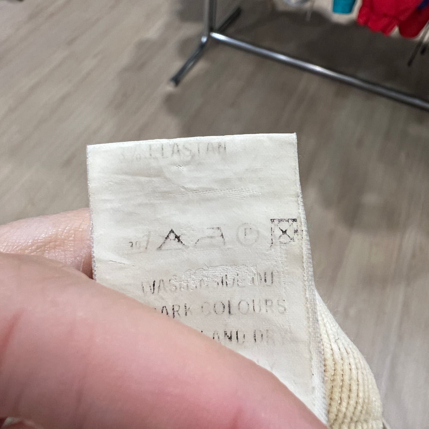 Close-up of a worn white care label on beige corduroy pants, showing faded washing symbols and partially legible text held between two fingers