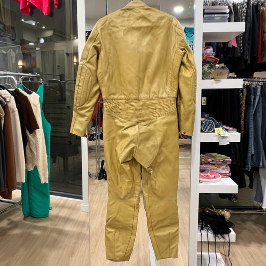 Full view of a yellow vintage work-style jumpsuit with zip pockets, padded knee panels, and a high collar, displayed on a hanger inside a vintage clothing store
