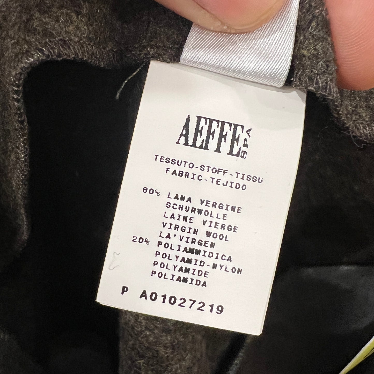 Close-up of an Aeffe fabric label inside a wool garment, listing 80% virgin wool and 20% polyamide in multiple languages, held between two fingers