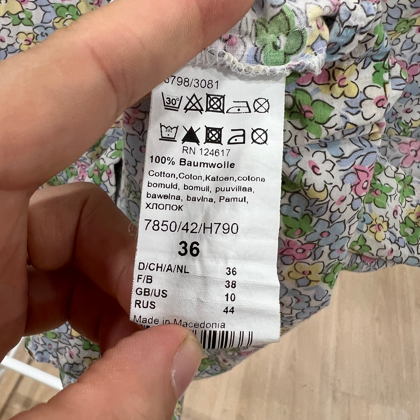 Clothing label held by a hand with floral fabric background