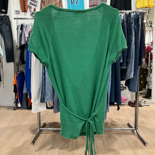 Green sweater with a tie front hanging on a rack in a clothing store