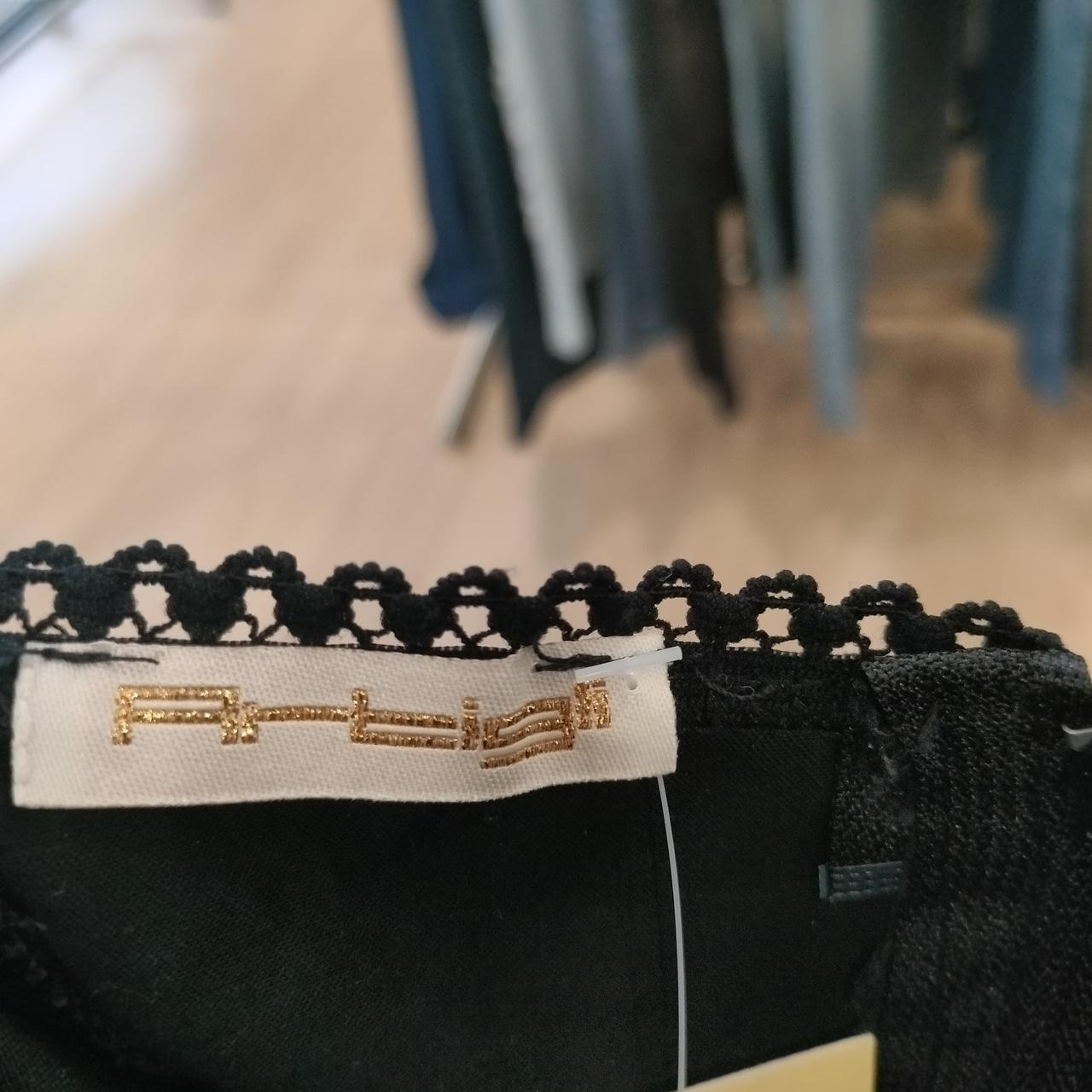 Close-up of black lace trim with gold embroidery on a garment, blurred background