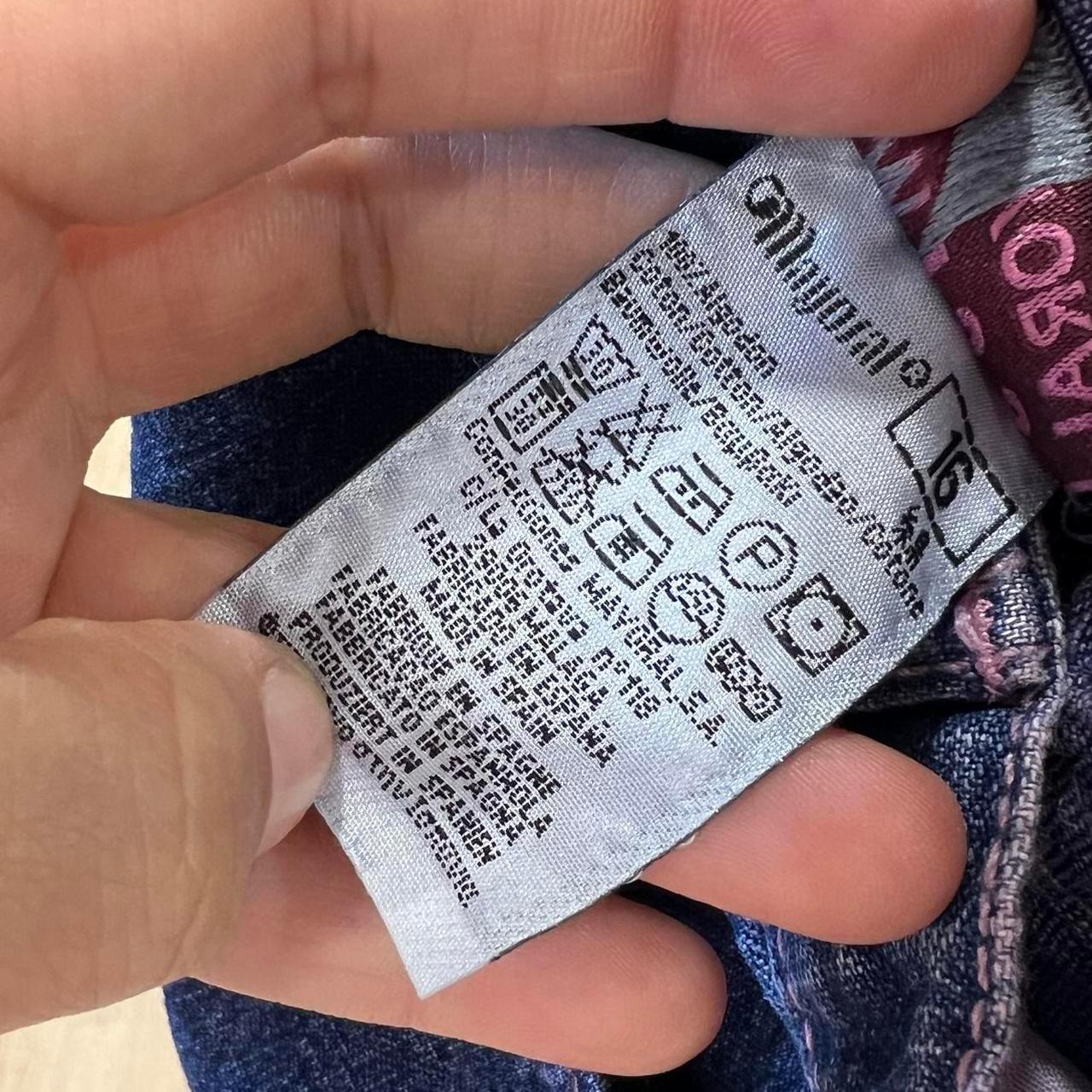 Close-up of a clothing care label with washing symbols, held near denim fabric.