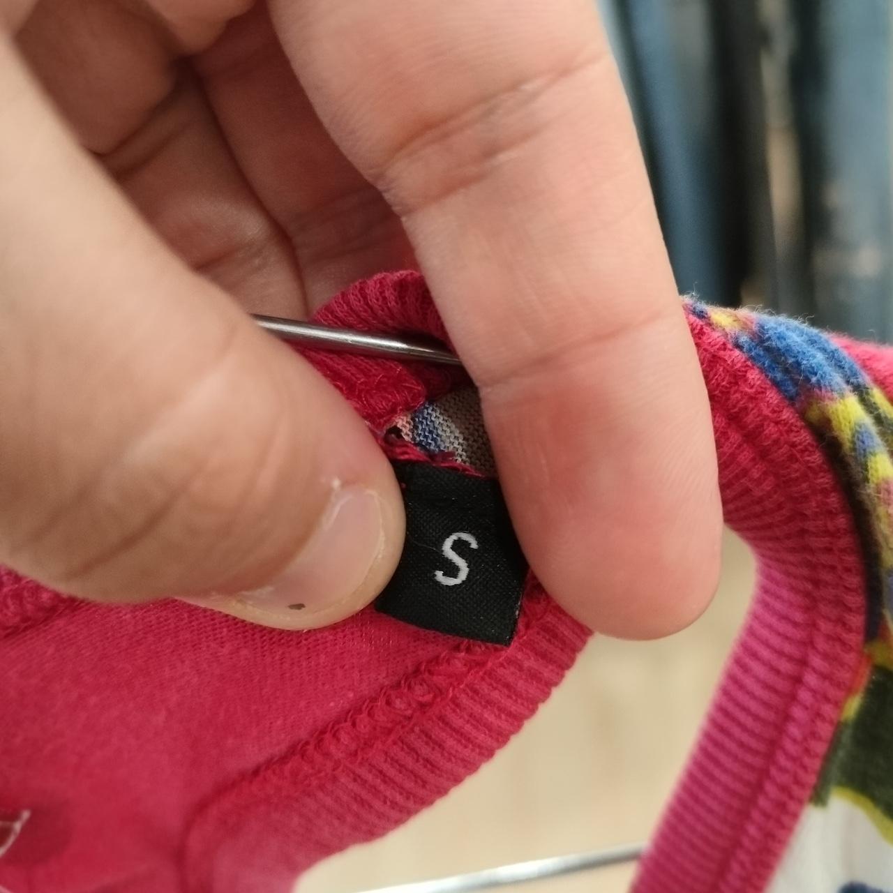 Close-up of a hand holding the size ‘S’ label on a pink garment