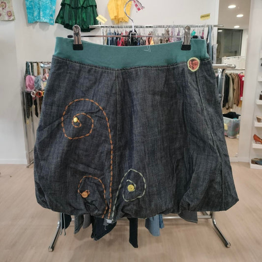 Dark denim A-line skirt with colorful embroidered swirl designs, displayed in a thrift fashion store