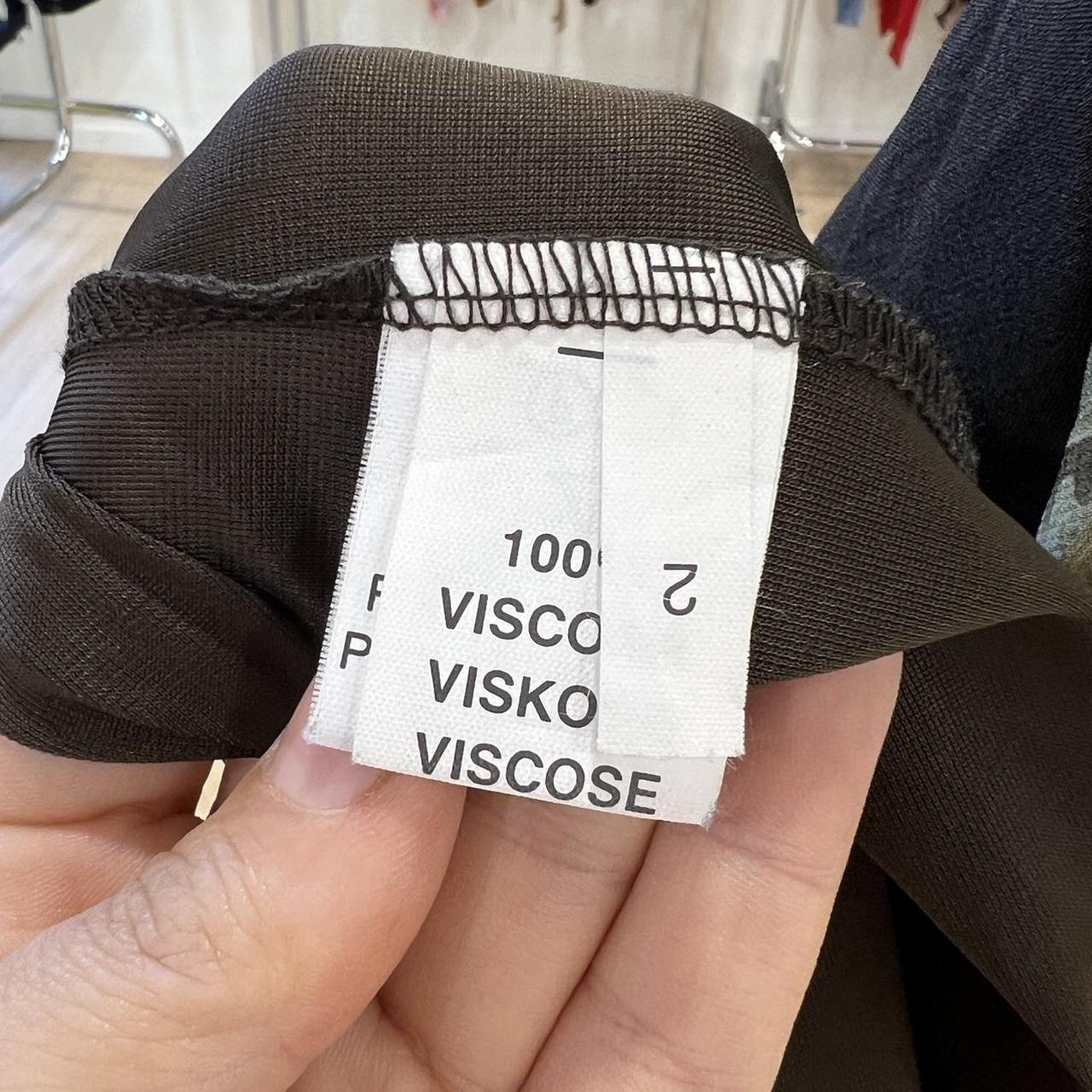 Hand holding brown garment with clothing label showing 100% viscose material