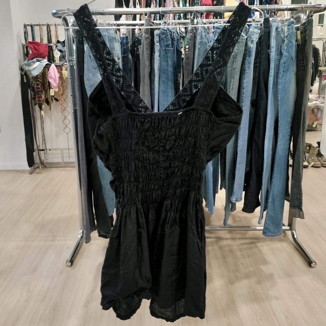 Black sleeveless smocked dress with lace straps on rack, surrounded by second hand jeans