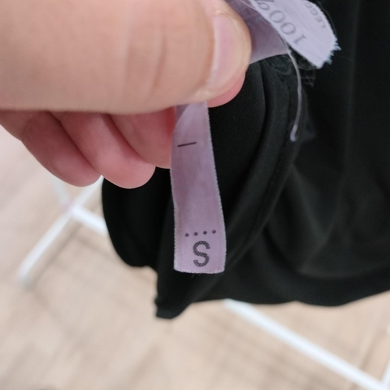 Black underwear with a size label held by a hand on a light background