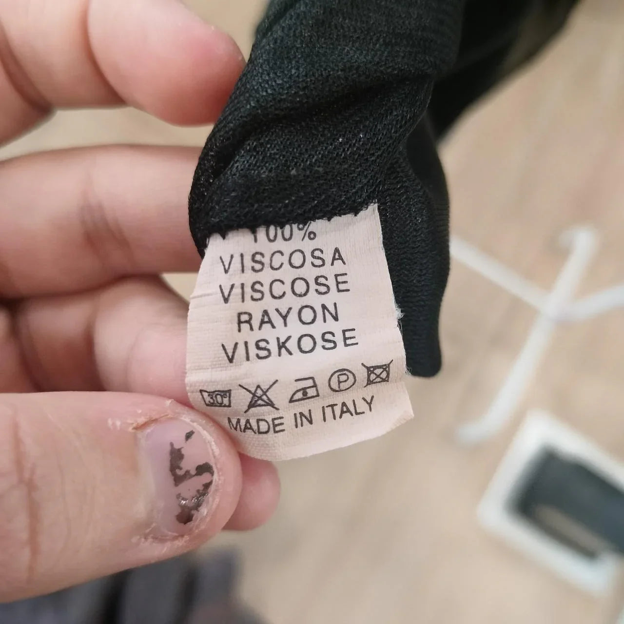 Clothing care label showing 100% viscose material and made in Italy, held by hand