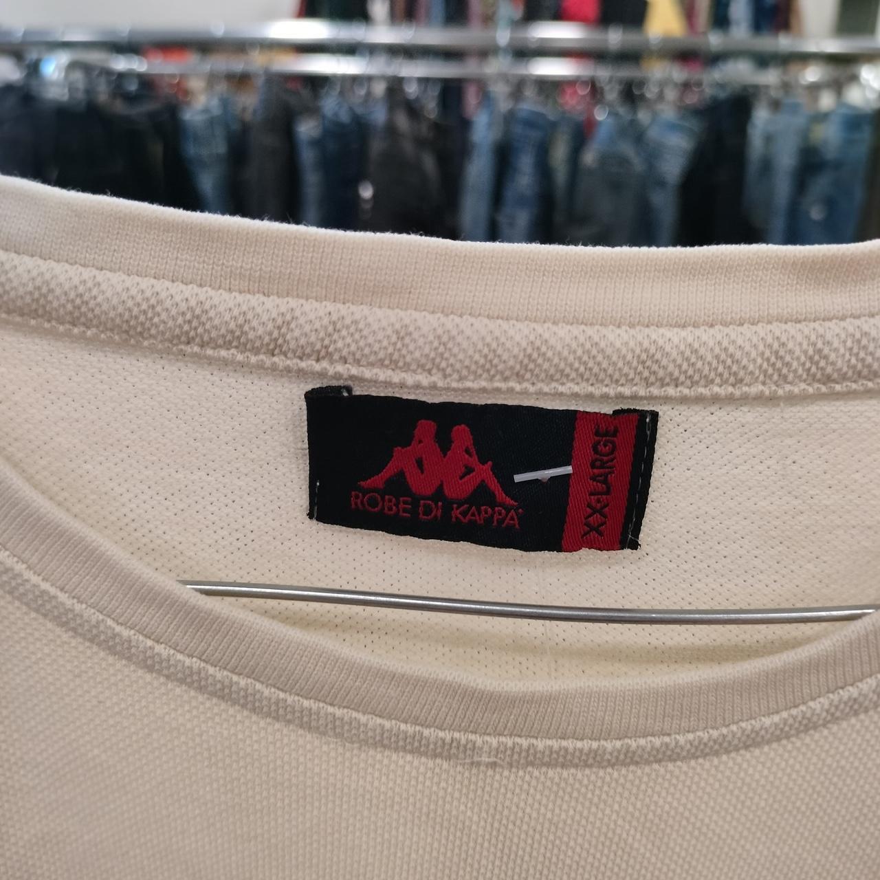 Close-up of a Kappa brand label on a beige garment with a clothing rack in the background
