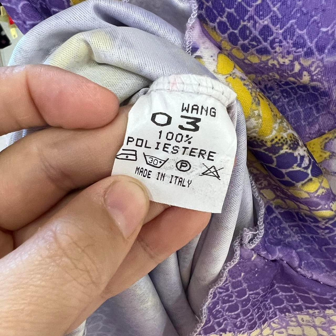 Hand holding clothing care label for purple and yellow patterned polyester fabric, made in Italy