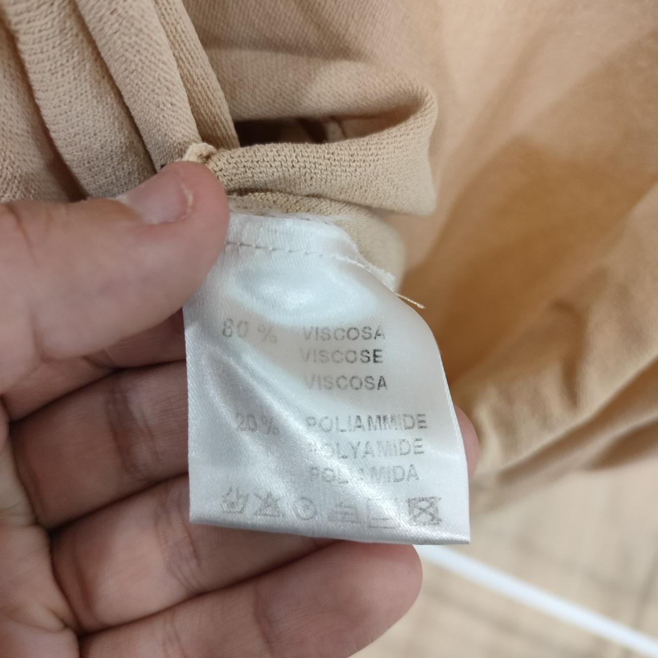 Hand holding a fabric tag with material information against beige fabric background