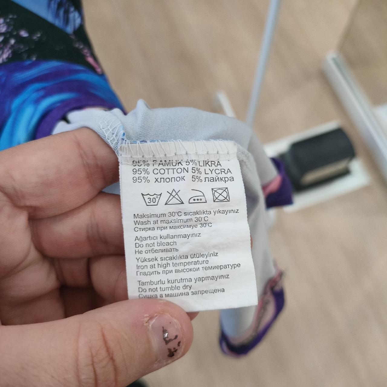 Hand holding clothing care label for 95% cotton 5% lycra leggings with wash instructions
