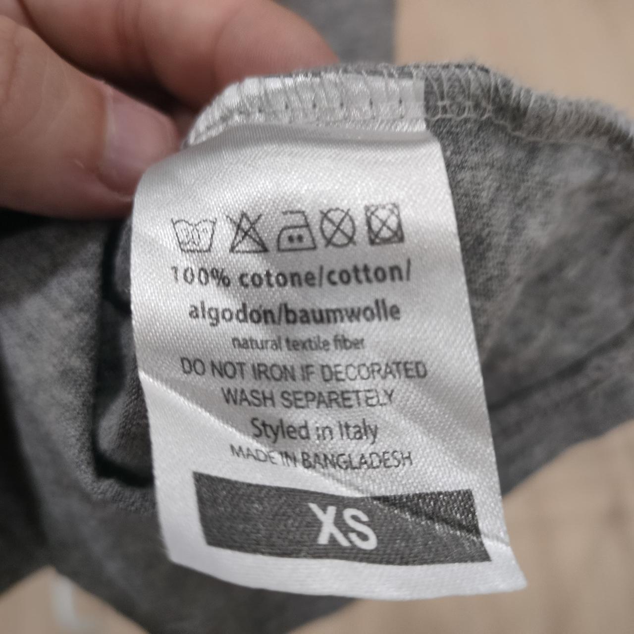 Tag on grey cotton garment showing size XS, material, and care instructions