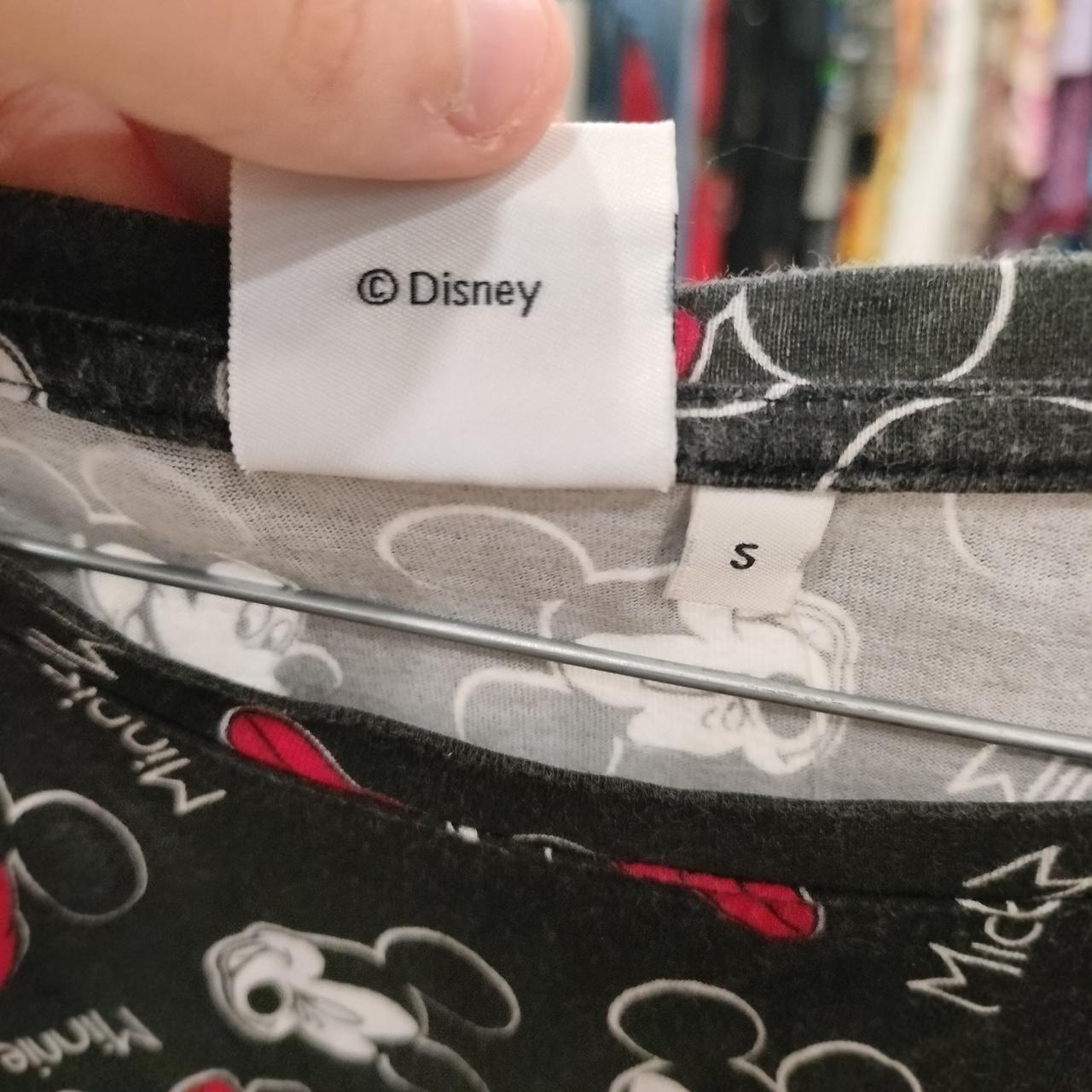 Hand holding Disney size S black Mickey Mouse print shirt in thrift shop