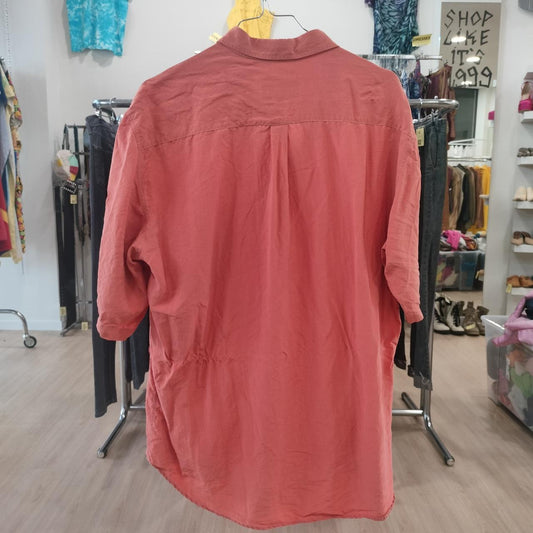 Red shirt on a hanger in a store setting with clothing racks and shelves in the background
