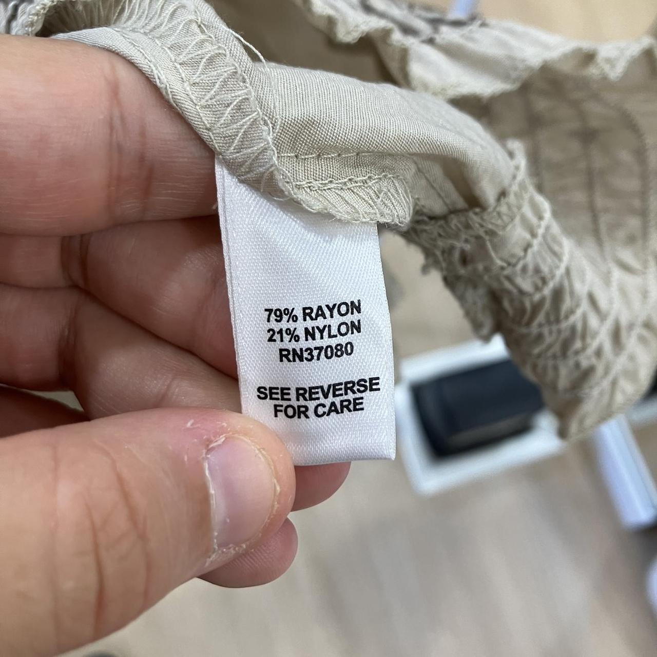 Clothing care label showing 79% rayon, 21% nylon fabric content in beige garment